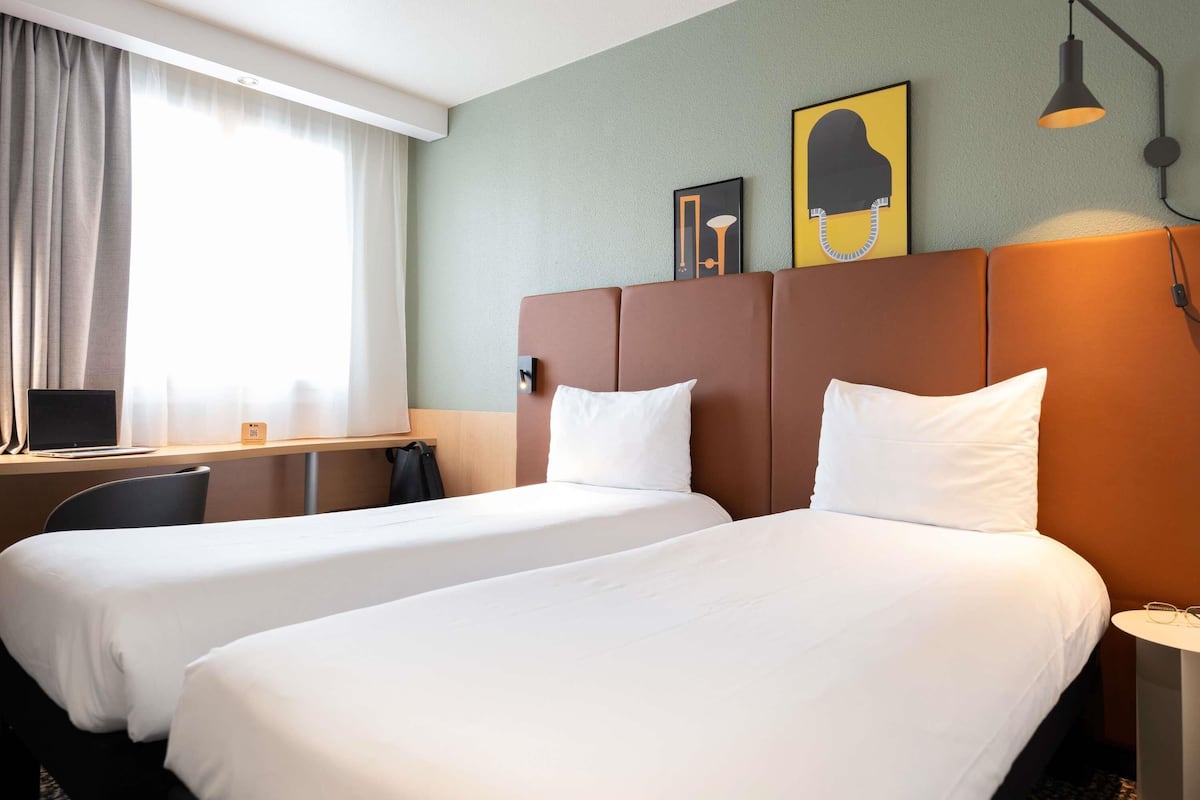 A hotel room with two beds, a desk, a laptop, and a lamp.