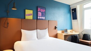A hotel room with a large bed, a desk with a laptop, a chair, and a small round table. There are two wall art pieces and a lamp. - ibis Paris Gare de Lyon Ledru Rollin 12ème (Paris)