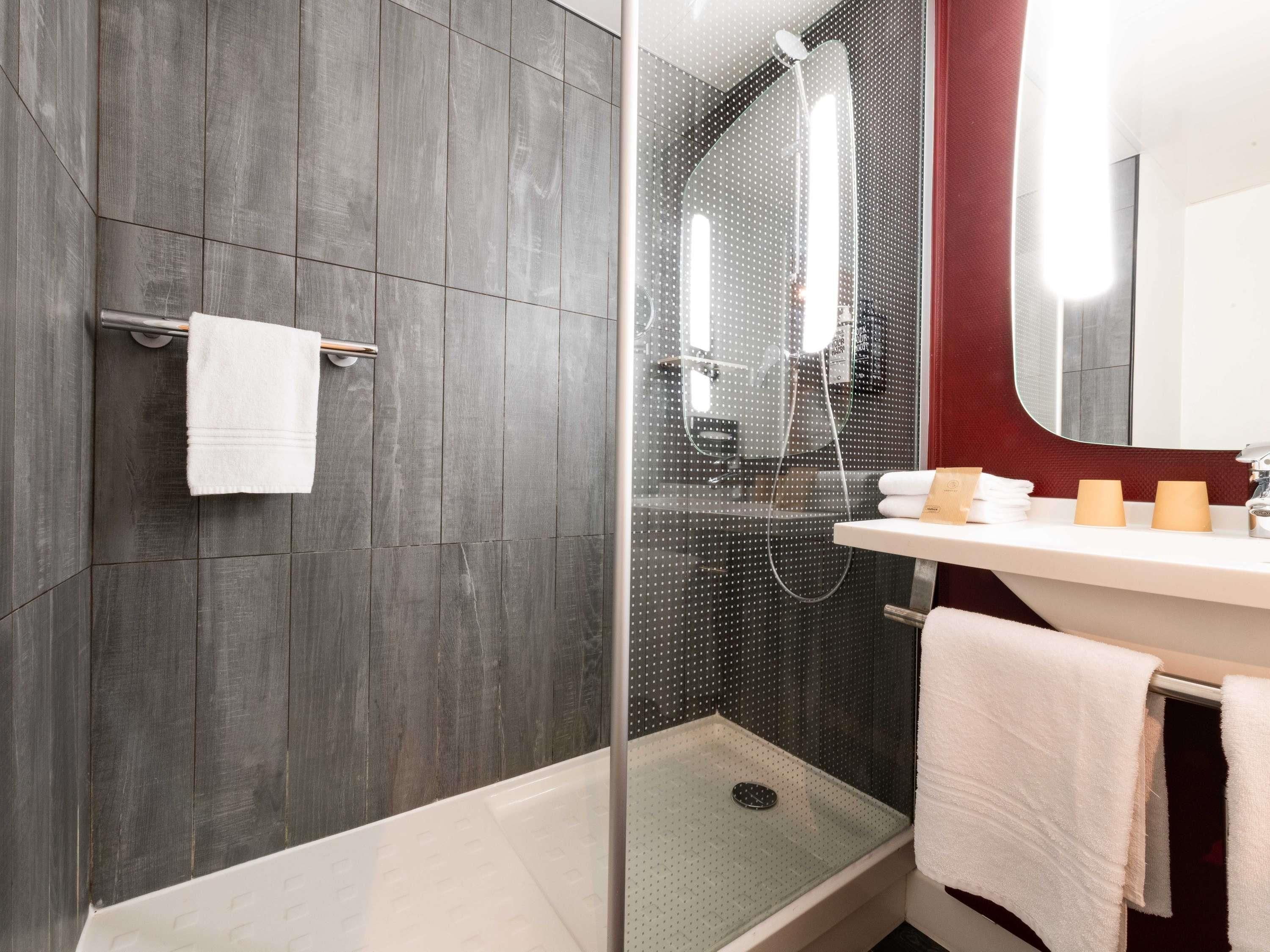 Un baño moderno con cabina de ducha de vidrio, un lavamanos blanco y una pared de acento roja.