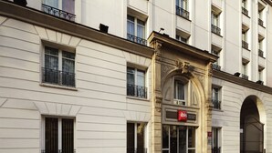 Un edificio con fachada clásica, una entrada destacada con arco y el letrero del hotel 'ibis'.