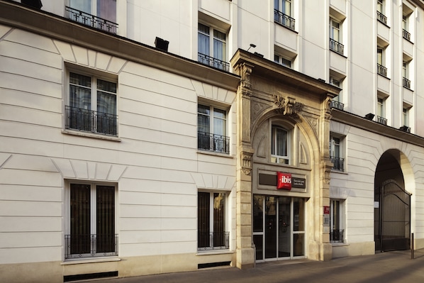 Ein Gebäude mit einer klassischen Fassade, einem markanten Eingang mit Bogen und einem Schild für das Hotel ibis.