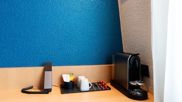 Una estación de café con cafetera, tazas y cargador de teléfono.