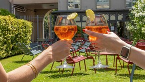 Two people toasting with drinks, a green hedge, and a building with windows in the background. - ibis Paris Gare de Lyon Ledru Rollin 12ème (Paris)