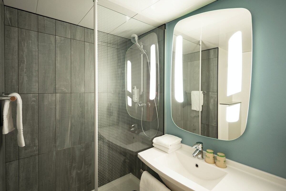 Un baño moderno con cabina de ducha de vidrio, un lavabo blanco y un espejo grande.