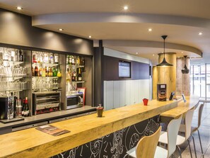 A modern bar area with a wooden counter, shelves with various bottles, and a digital screen displaying a menu. - ibis Paris Gare de Lyon Ledru Rollin 12ème (Paris)