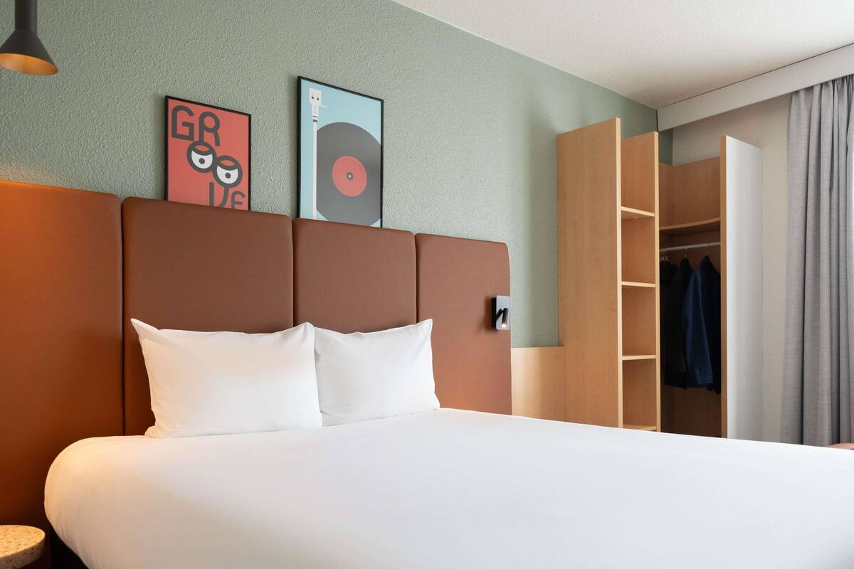 A hotel room with a bed, a headboard, a wardrobe, and two wall art pieces.