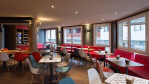 Un restaurant moderne avec des banquettes et des tables rouges, de grandes fenêtres et un plancher en bois.