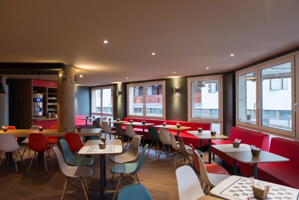 Un restaurant moderne avec des banquettes et des tables rouges, de grandes fenêtres et un plancher en bois.