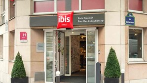 L’entrée d’un hôtel, avec une enseigne rouge représentant un ibis, un panneau indiquant « Paris Brancion » et une adresse au 15, avenue.