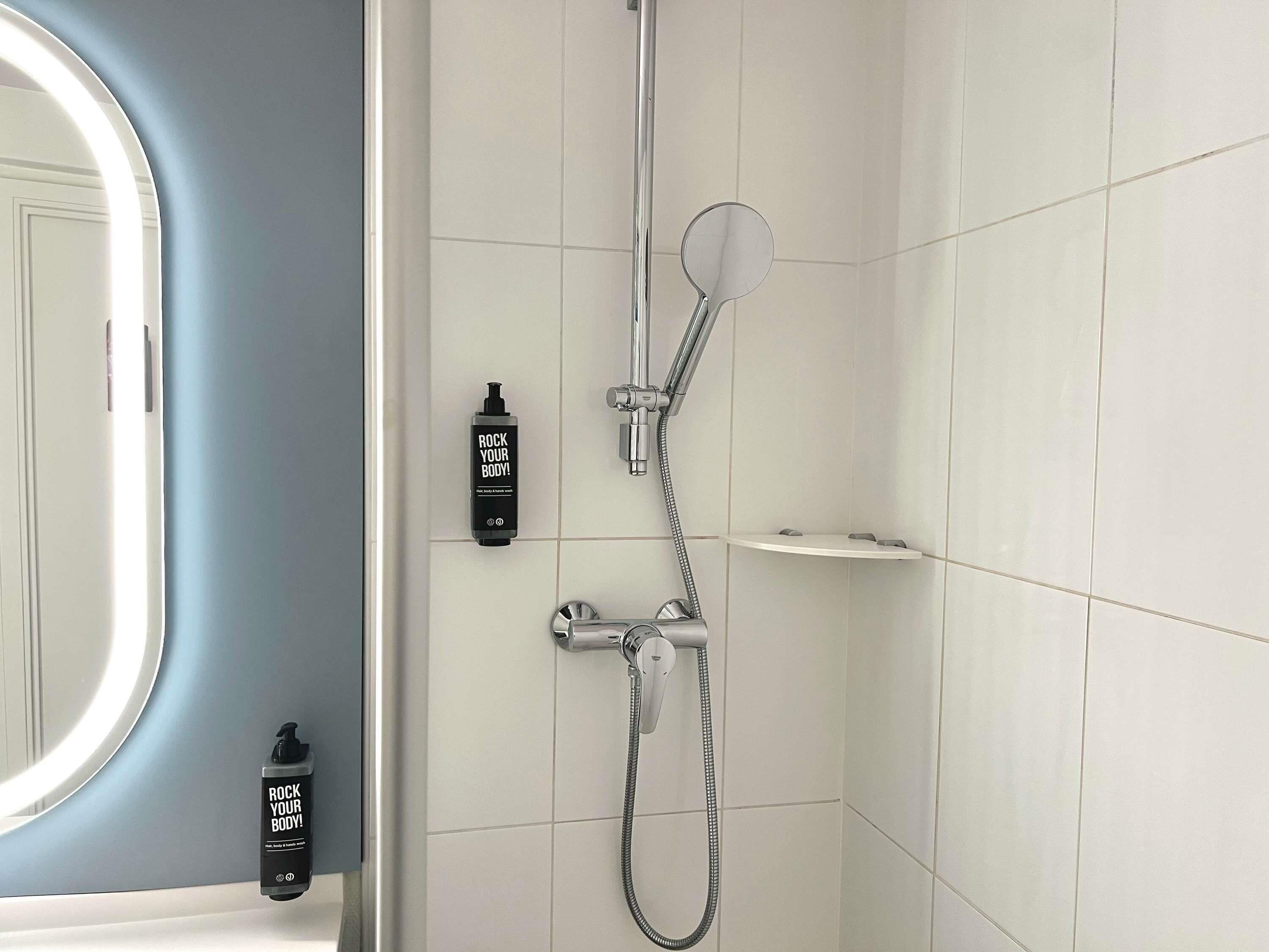 Un baño con ducha, espejo y dos botellas de crema corporal.