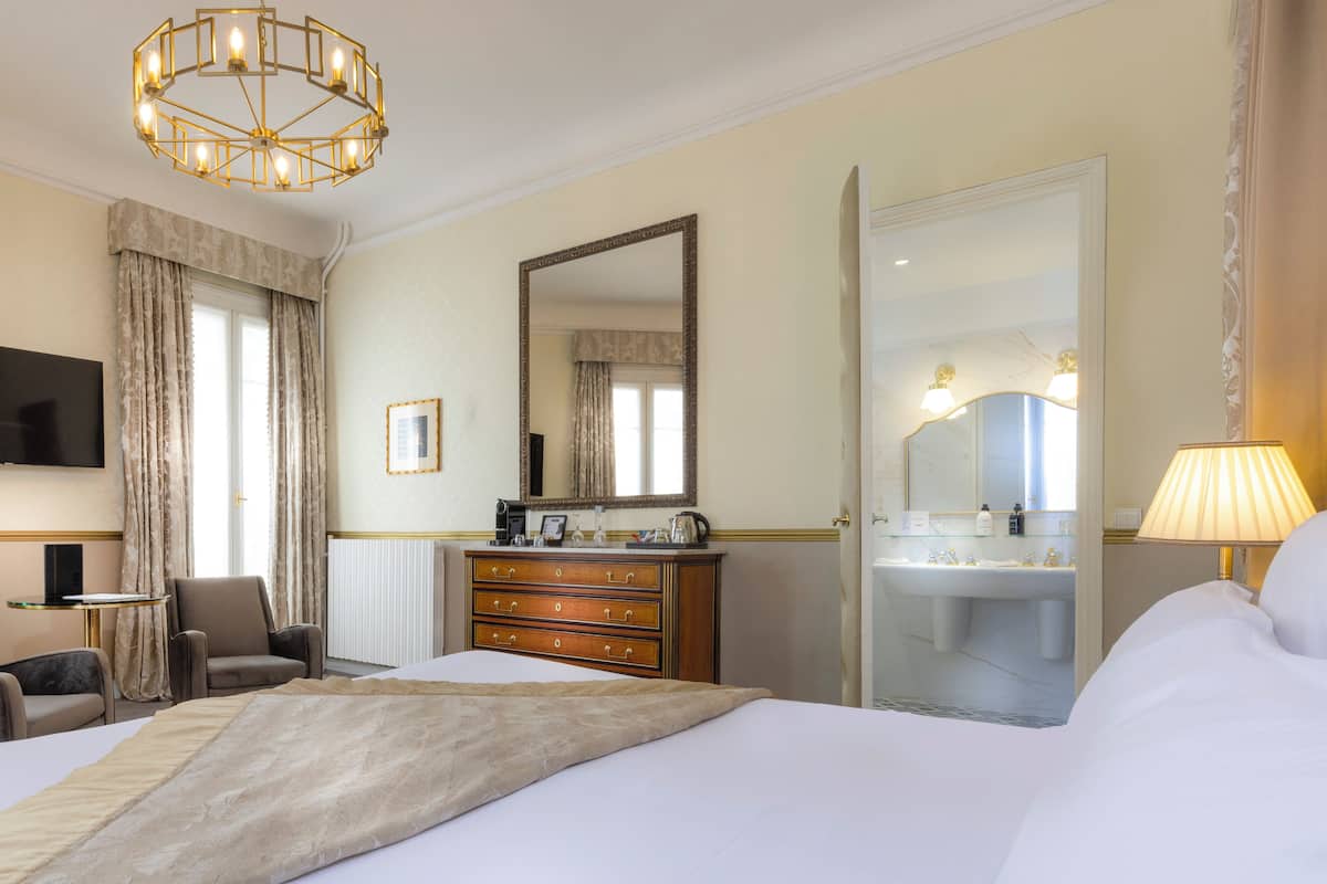 A hotel room with a large bed, a dresser, a chair, a television, and a bathroom visible through an open door.