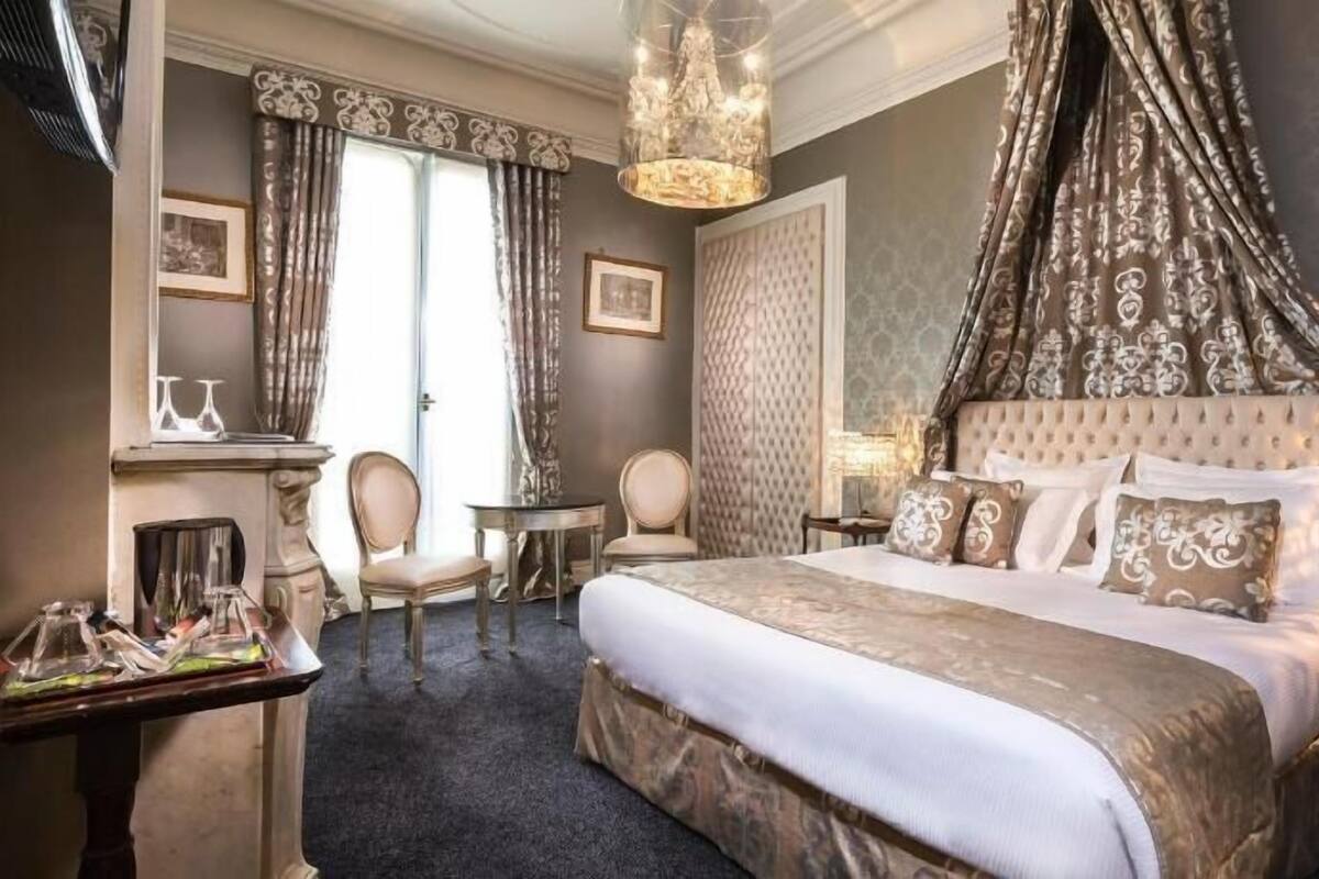 A hotel room with a large bed, a sitting area with chairs, a small table, and a chandelier.