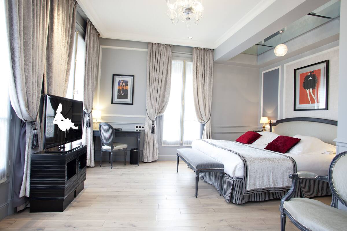 Ein Hotelzimmer mit einem Bett, einem Schreibtisch, einem Sessel, einem Fernseher und einer Bank.