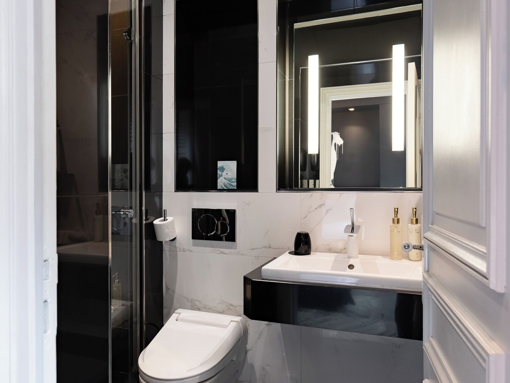 Une salle de bain moderne avec une douche à parois de verre, des toilettes blanches, un meuble-lavabo noir et blanc et un grand miroir.