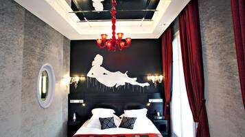 A modern hotel room with a large bed, a chandelier, and a unique wall art piece.
