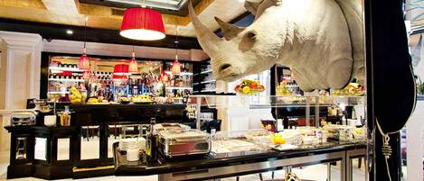 Een bar met een groot decoratiebeeld van een neushoorn, een toonbank met diverse etenswaren, en planken vol flessen en snacks.