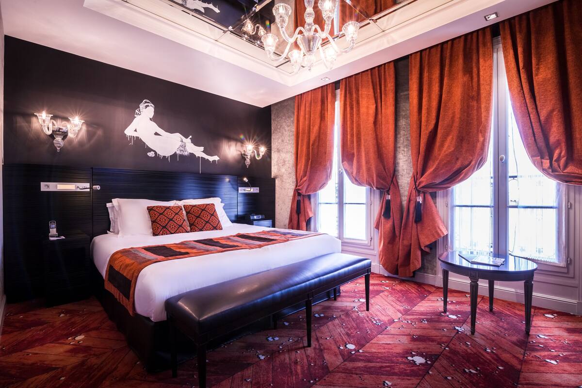 Ein modernes Hotelzimmer mit einem großen Bett, einer Bank, einem kleinen Tisch und einer Kandelaber.