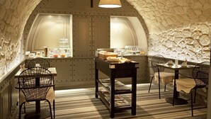 A cozy, arched room with a stone wall, a wooden table, and four chairs. - Hotel Therese (Paris)
