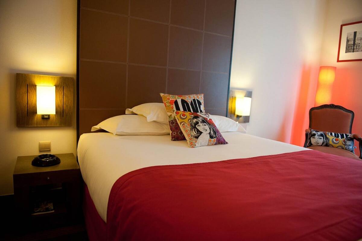 A hotel room with a neatly made bed, two bedside lamps, a chair, and a nightstand with a lamp.