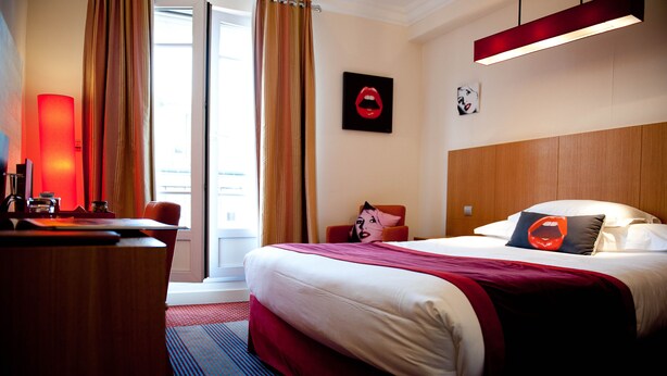 A hotel room with a large bed, a desk, and a window with curtains. - Hôtel Westside Arc de Triomphe (Paris)