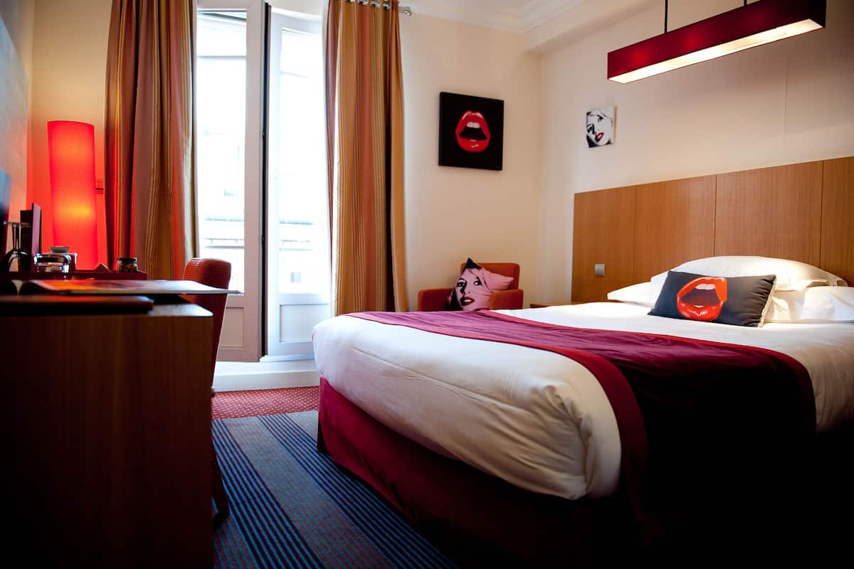 A hotel room with a large bed, a desk, and a window with curtains.
