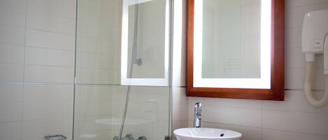 Un baño con ducha de vidrio, lavamanos blanco y tocador de madera.