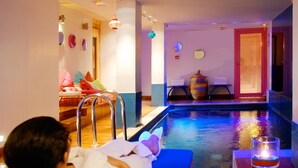 A person relaxing by a poolside lounge chair with a view of a pool and a room with a door, a table, and a colorful vase. - Hôtel Westside Arc de Triomphe (Paris)