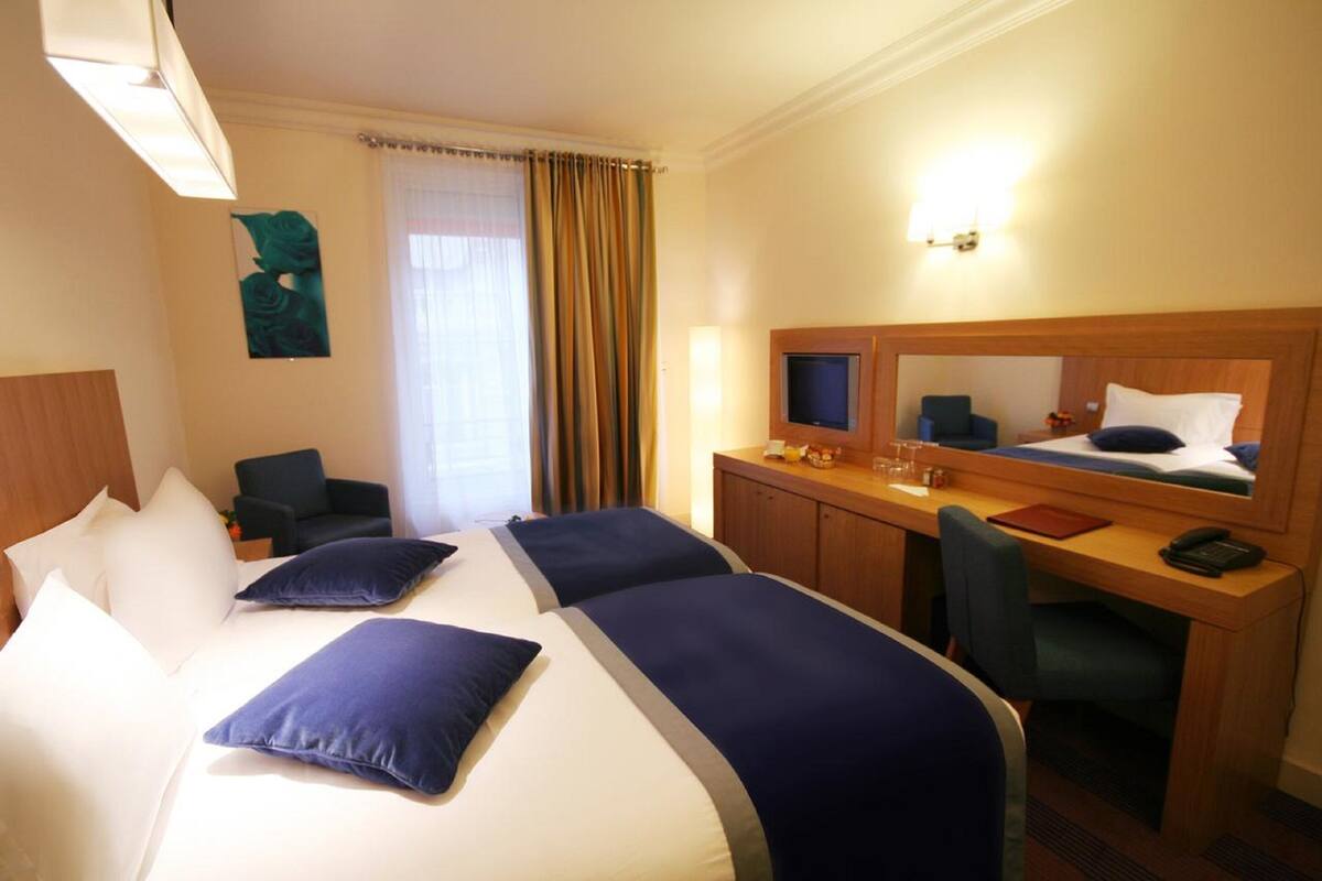 A hotel room with two beds, a desk, a chair, a TV, and a mirror.