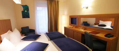 A hotel room with two beds, a desk, a chair, a TV, and a mirror.