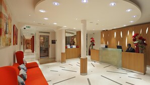 A modern hotel lobby with a reception desk, a red seating area, and a staircase in the background. - Hôtel Westside Arc de Triomphe (Paris)