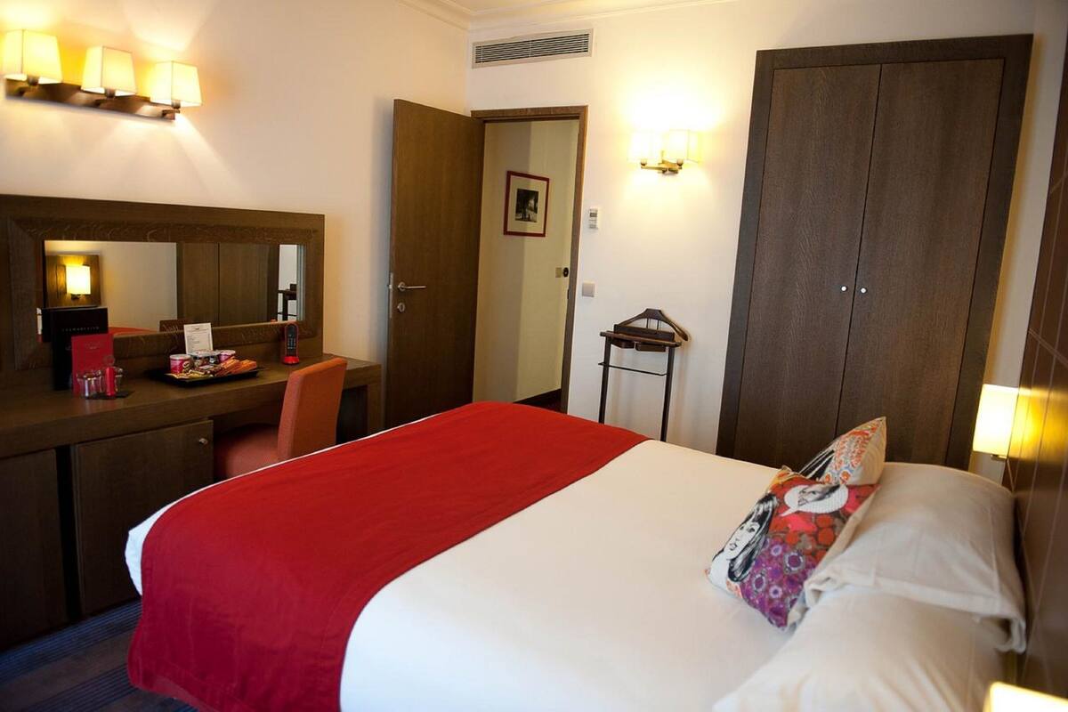 A hotel room with a bed, a desk, a chair, a mirror, and a wardrobe.