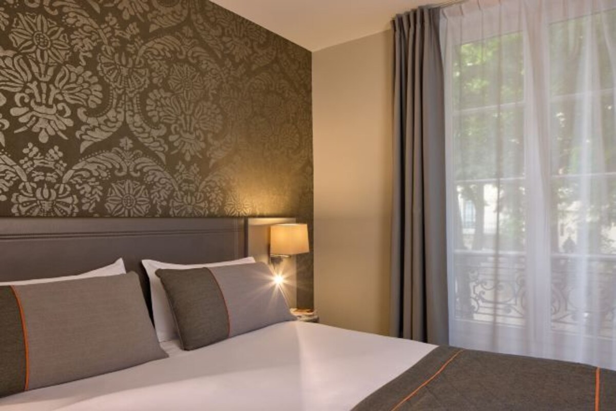 Una habitación de hotel con una cama grande, una mesita de noche con lámpara y una ventana con cortinas.