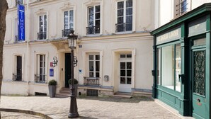 Ein historisches Gebäude mit einer klassischen Fassade, einem markanten Eingang und einer grünen Schaufensterfront.
