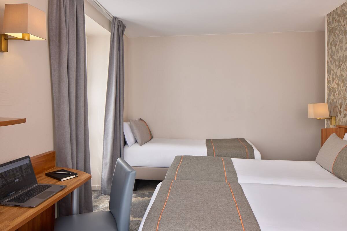 Une chambre d’hôtel avec deux lits, un bureau avec un ordinateur portable et une chaise.