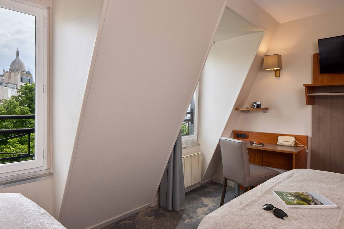 Une chambre d’hôtel équipée d’un lit, d’un bureau, d’une chaise, d’une télévision et offrant une vue sur un bâtiment surmonté d’un dôme.