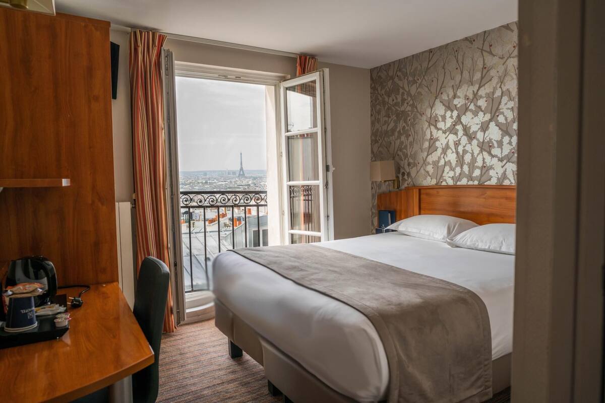 Une chambre d’hôtel avec un lit, un bureau et une vue sur la Tour Eiffel.