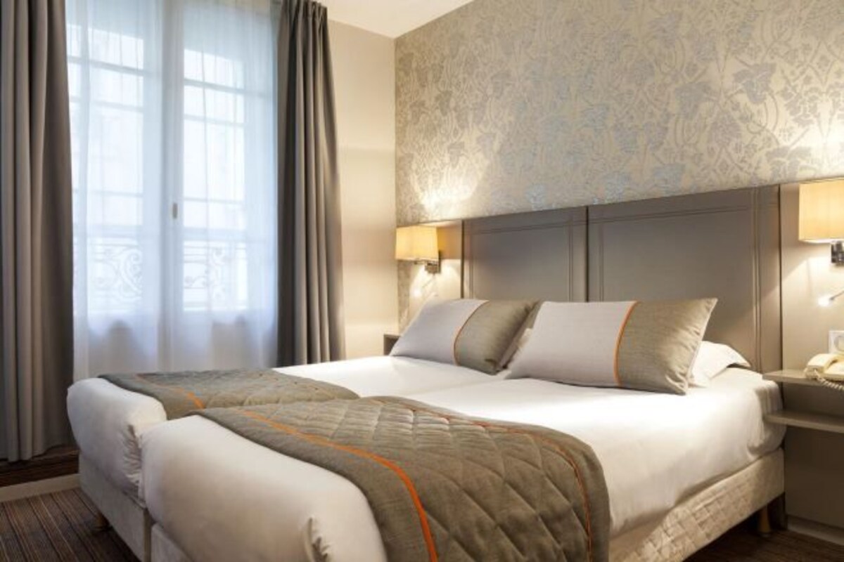 Habitación de hotel con una cama grande, dos mesitas de noche y vistas a un paisaje urbano a través de la ventana.