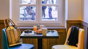 Ein Zimmer mit Fenster zur Straße, ein Tisch mit Stuhl, eine Handtasche, eine Tasse und ein Teller mit Essen.