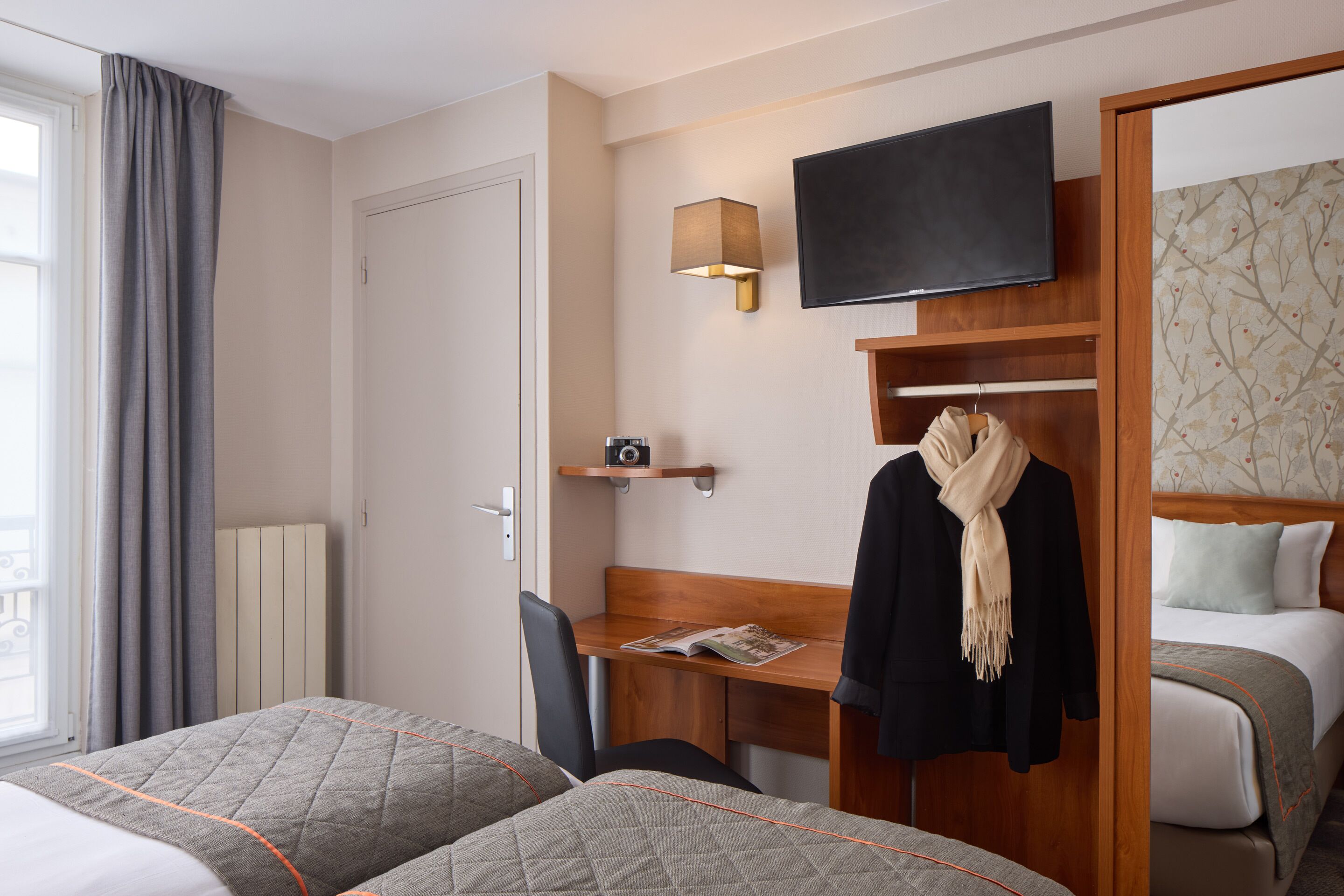 A hotel room with two beds, a desk with a chair, a TV mounted above the desk, and a wardrobe.