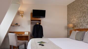 Habitación de hotel con cama, escritorio, silla, televisor montado en la pared y perchero.