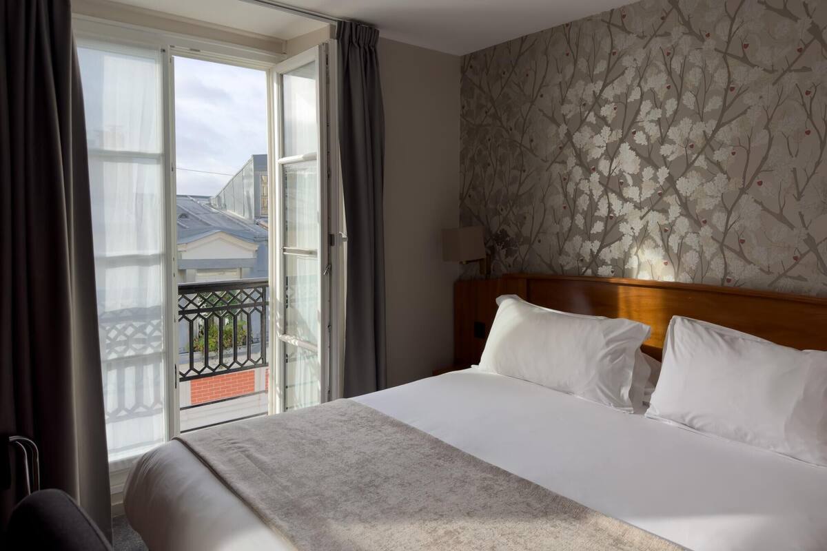 Une chambre d’hôtel avec un grand lit, une tête de lit en bois et une vue sur un balcon doté d ’une balustrade.
