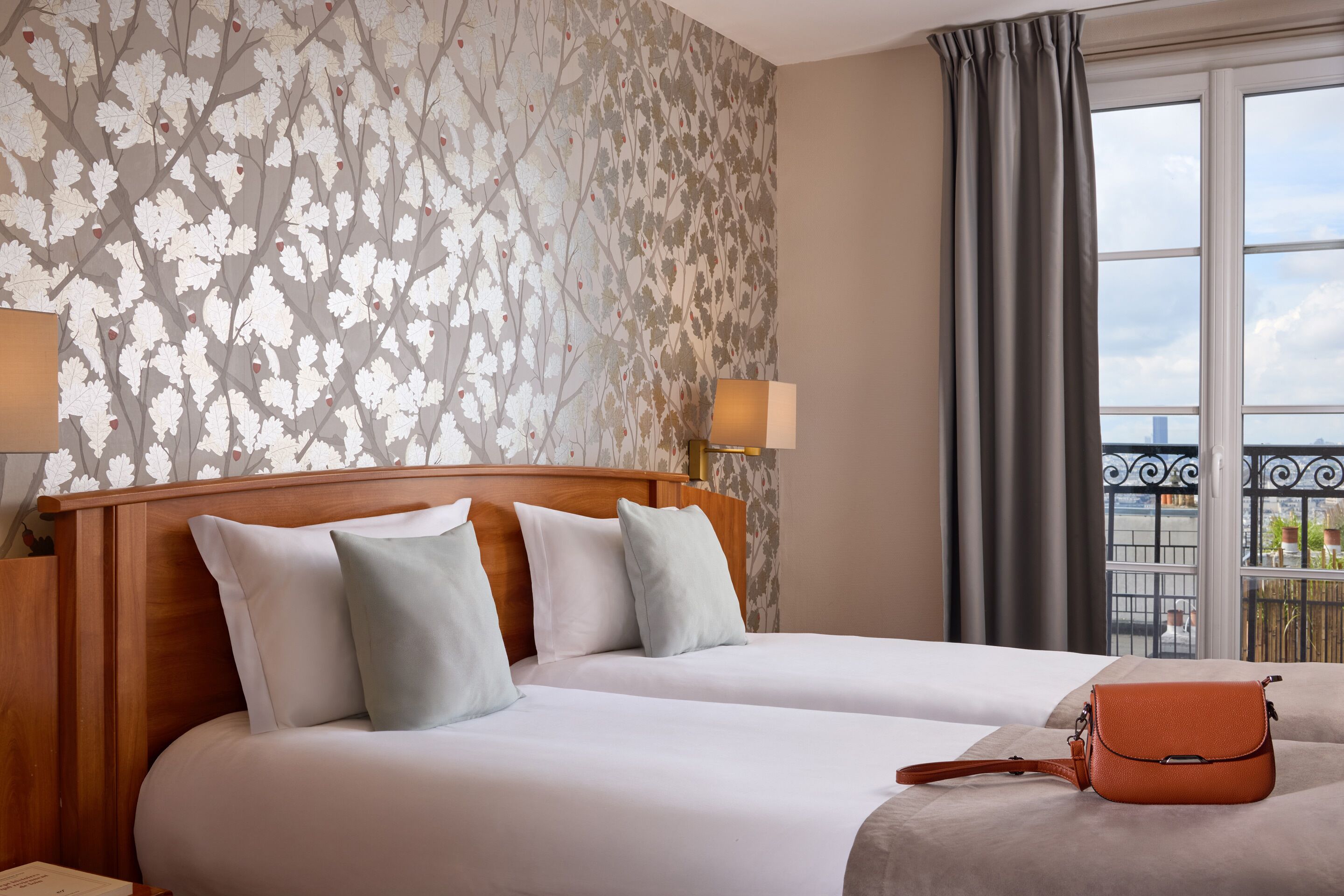 A hotel room with a large bed, two pillows, a wooden headboard, a window with curtains, and a view of the city.