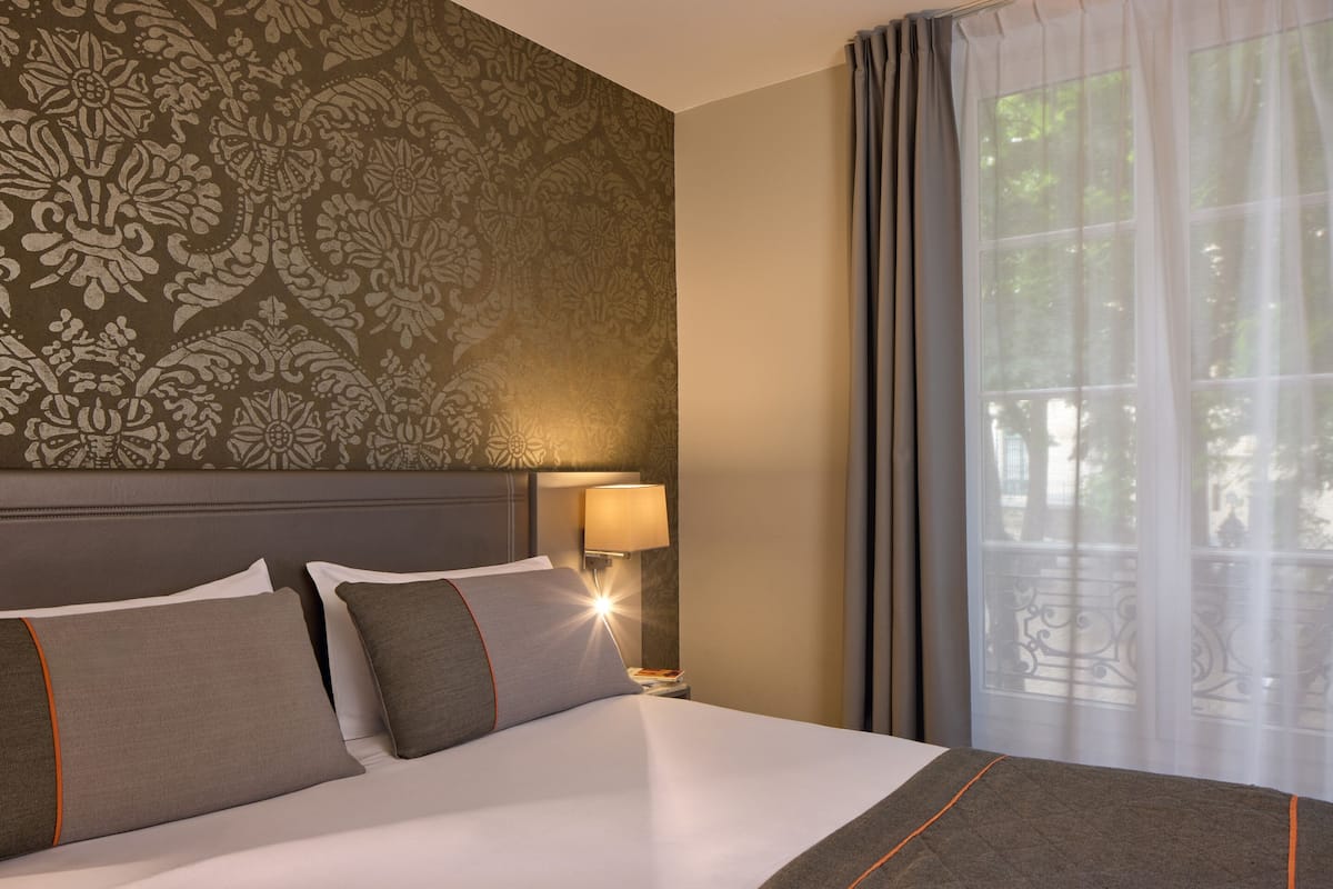 Une chambre d’hôtel avec un grand lit, une table de chevet avec une lampe et une fenêtre avec des rideaux.