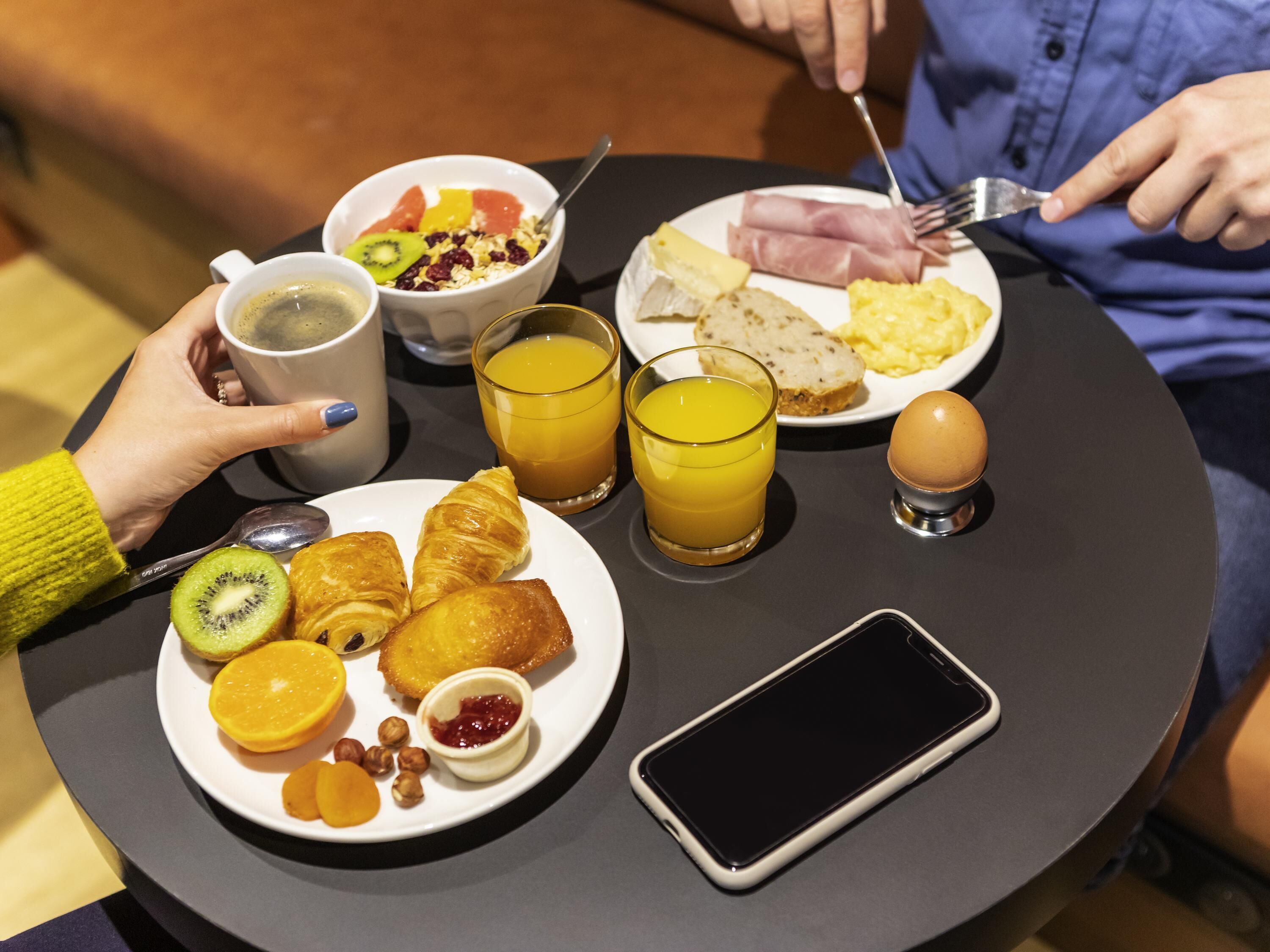 A breakfast setting with croissants, fruit, and a smartphone on a table.