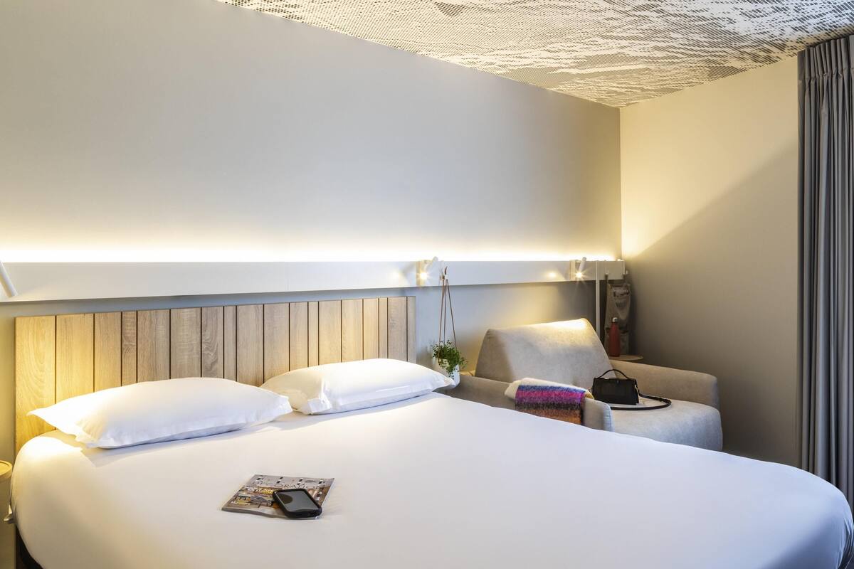 A hotel room with a large bed, bedside tables, a sofa, and a lamp.