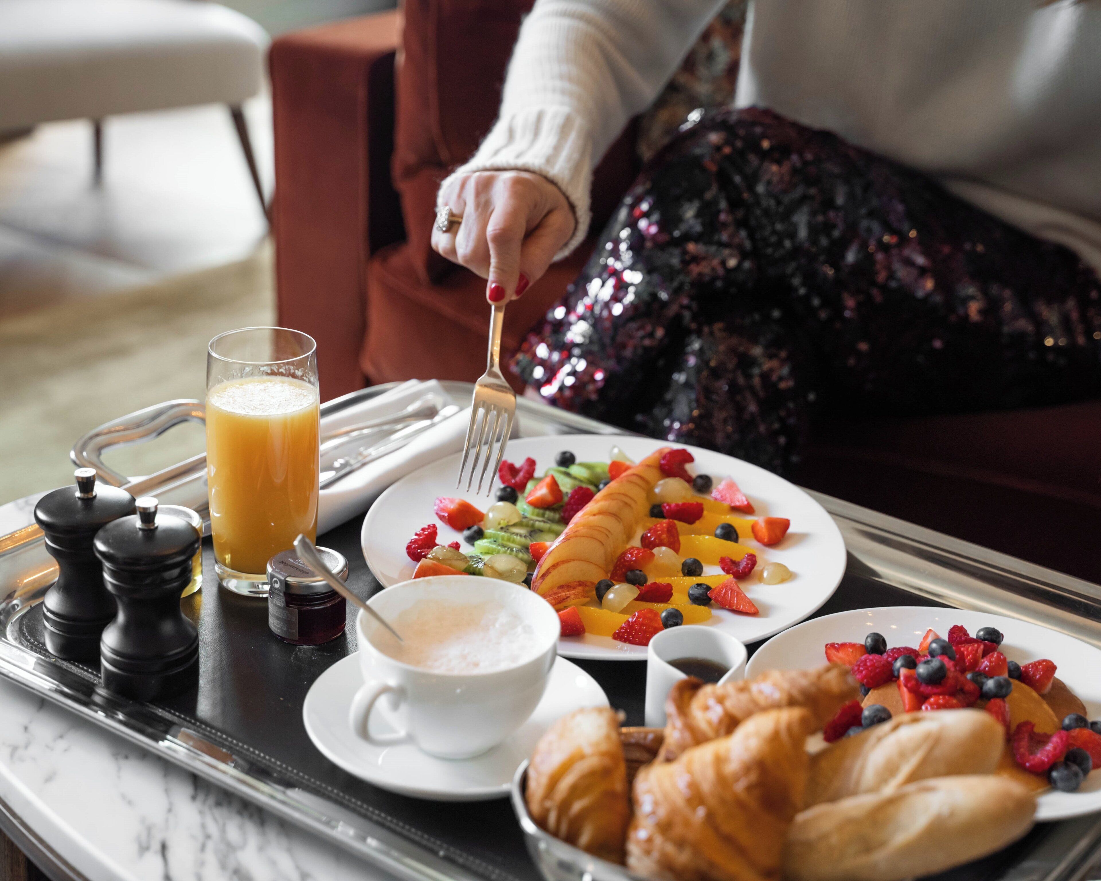 Bandeja de desayuno con croissants, fruta, un vaso de zumo de naranja y una taza de café.