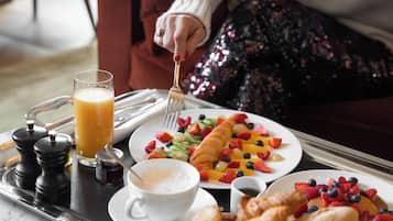 A breakfast tray with croissants, fruit, a glass of orange juice, and a cup of coffee.