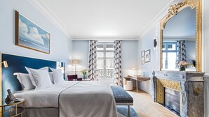 Une chambre d’hôtel avec un grand lit, un bureau, une cheminée et un grand miroir.