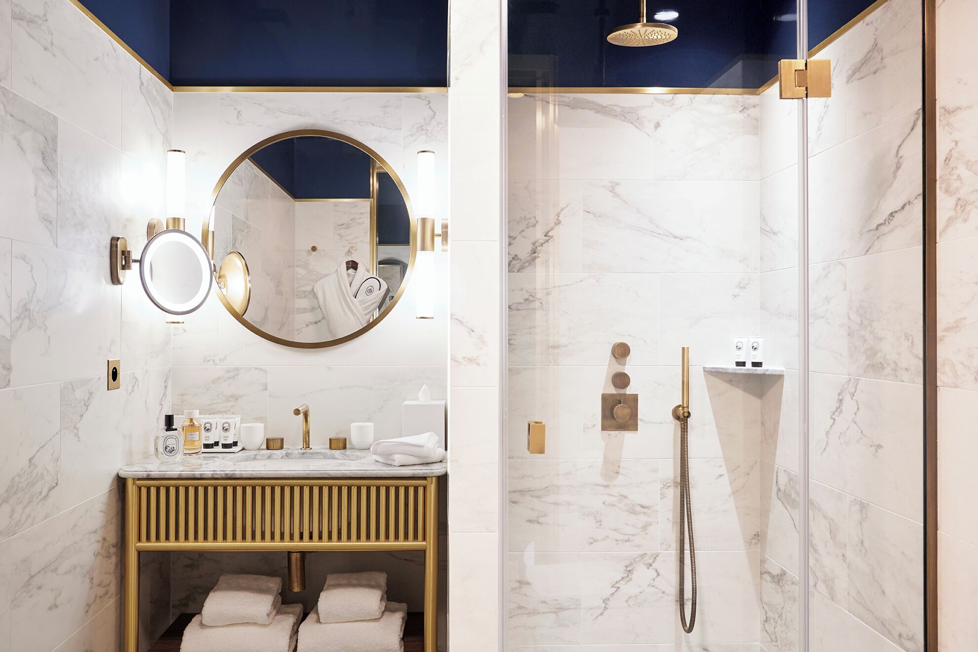 A modern bathroom with a marble vanity, a round mirror, a gold-framed shower enclosure, and a gold radiator.