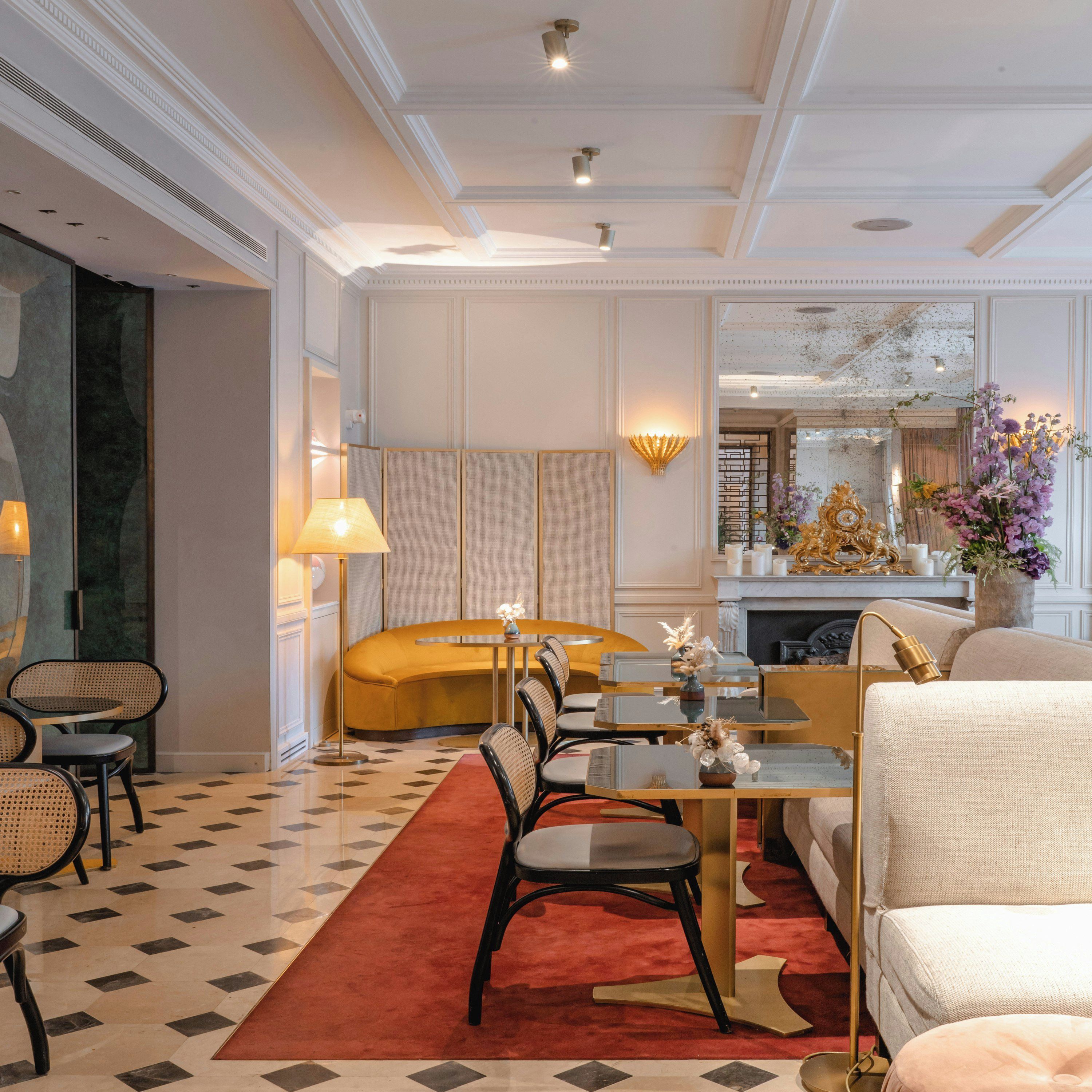 A hotel room with a dining area, a sofa, a fireplace, and a decorative vase with flowers.